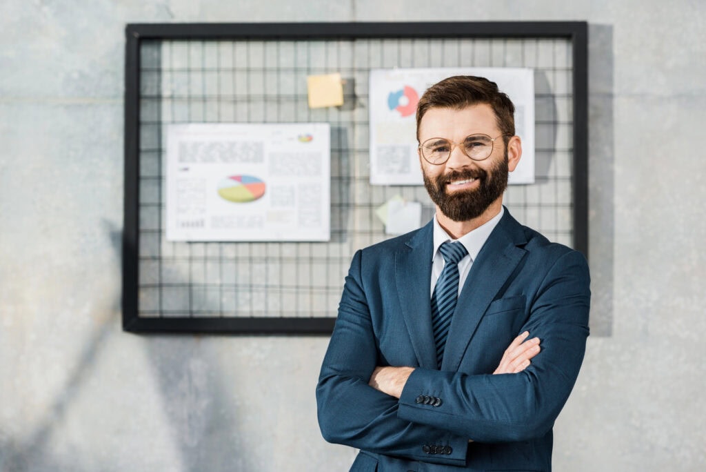 Businessman standing with crossed arms and smiling at camera in office