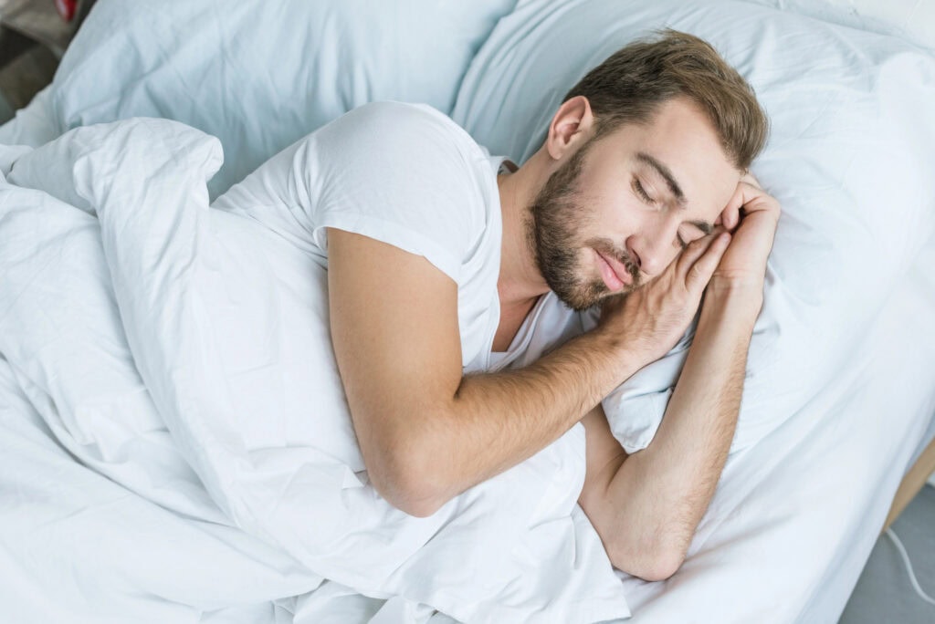 High angle view of handsome young man sleeping in bed