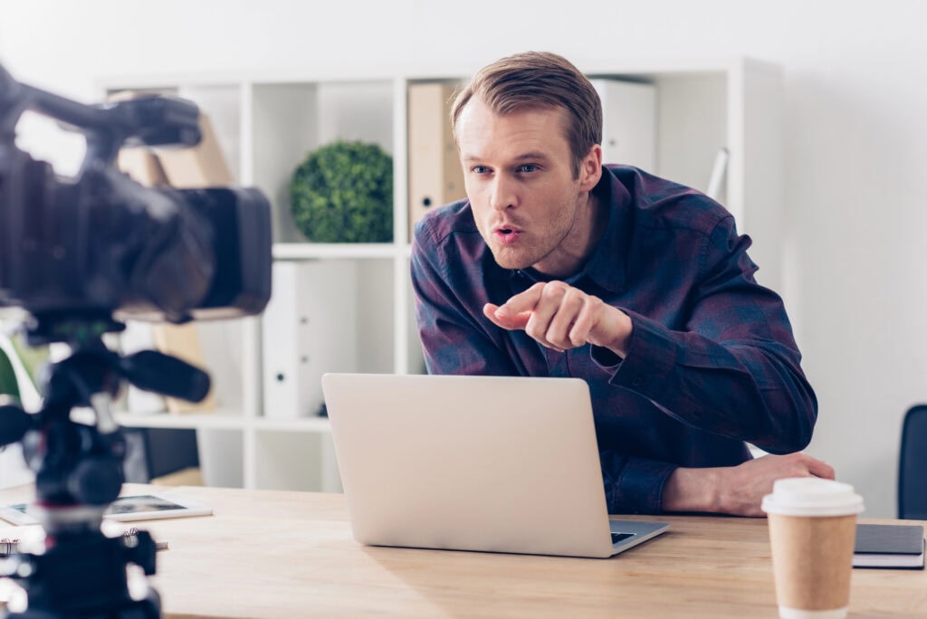 Aggressive male video blogger recording vlog and pointing on camera in office