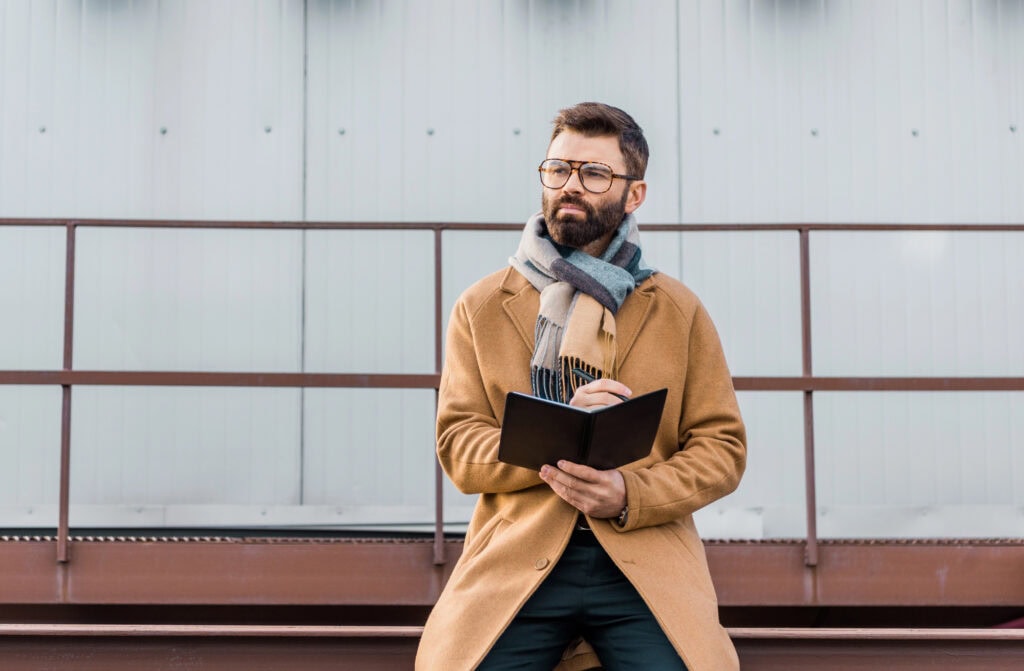 Businessman standing in coat and scarf with notebook and pen in hands