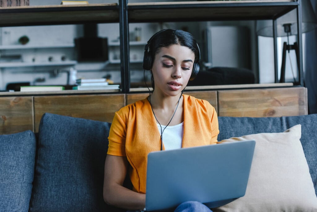 Beautiful mixed race girl in orange shirt listening music and using laptop in living room