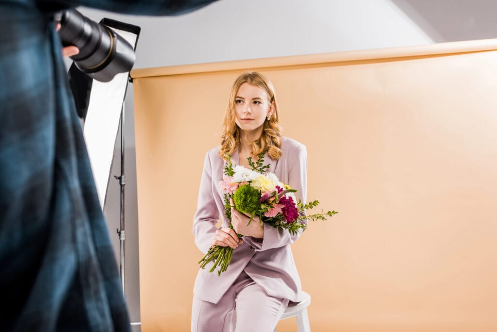 Cropped shot of photographer shooting young female model with flowers in photo studio
