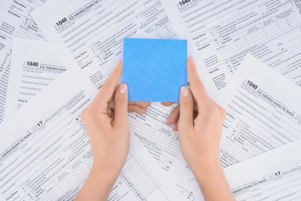 Cropped view of woman holding empty blue card with tax forms on background