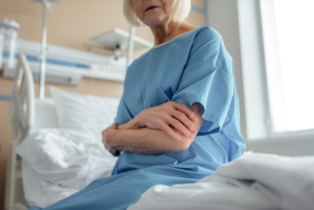 Cropped view of senior woman with arms crossed sitting on bed in hospital ward