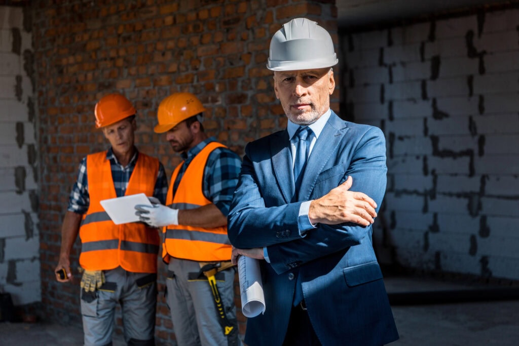 Selective focus of businessman standing with crossed arms near constructors
