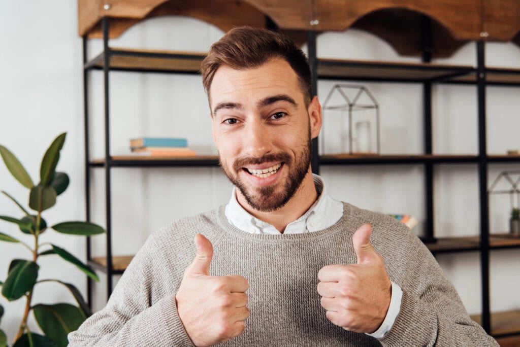 Handsome man showing thumbs up gesture and smiling at camera