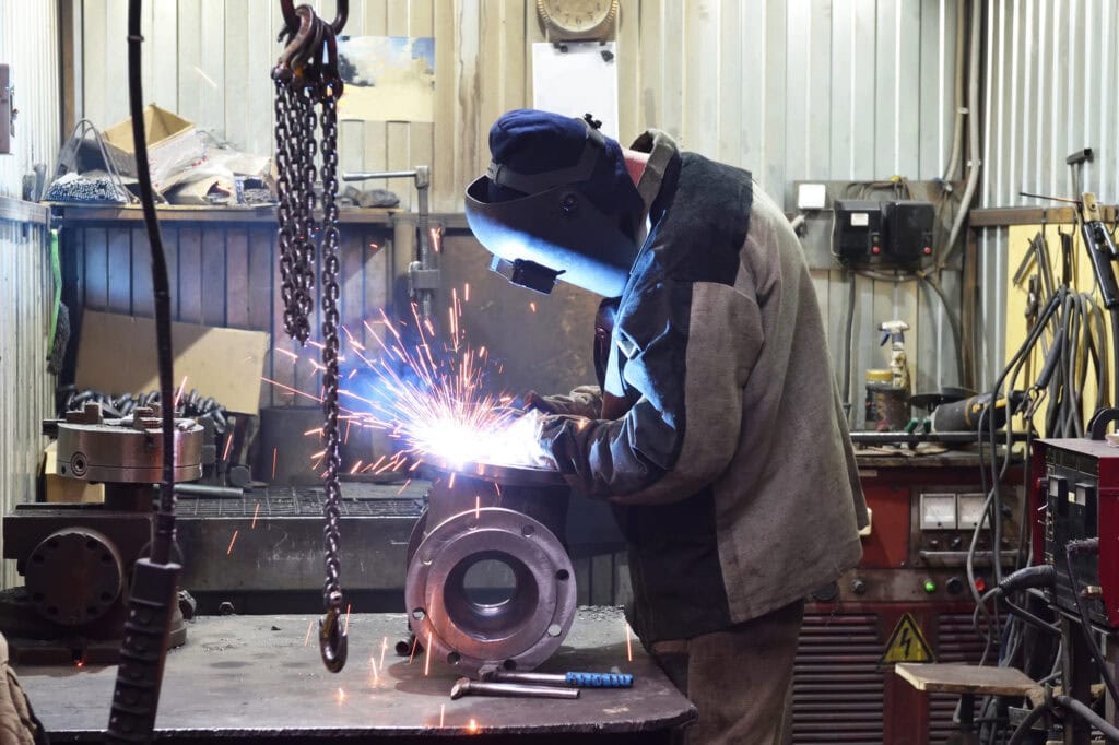 The base for the valvemounted on the iron table at the factory and the worker welding with welding machine. Sparks flying