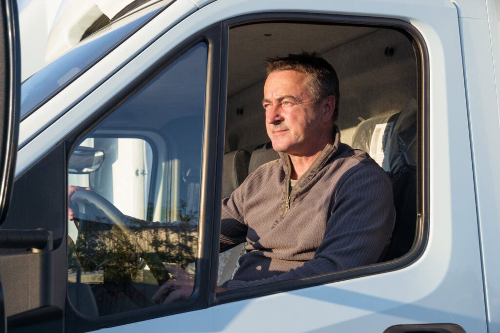 A man driver is sitting in the cab of a modern truck.