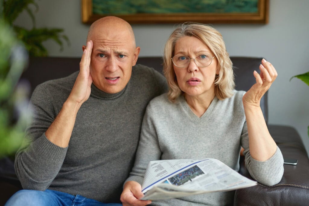 Adult woman and man reading newspaper.