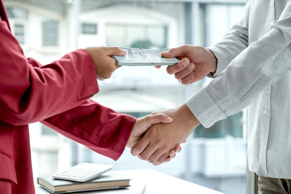 Photo of Businessmen shake hands and dollar note, sign a contract to bribe corruption in the company. The concept of bribery and corruption.