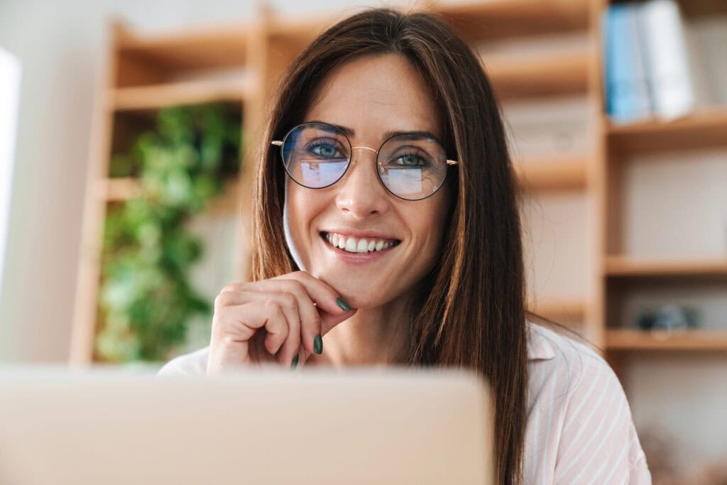 Happy woman in eyeglasses smiling while working with laptop at office