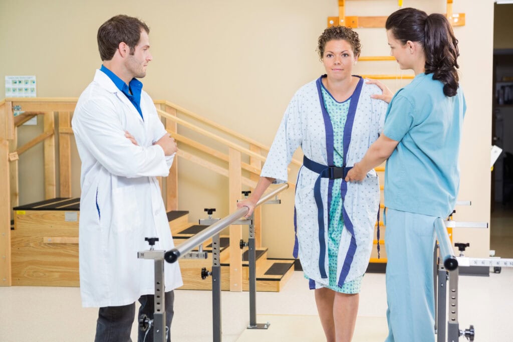 Physical Therapist With Doctor Assisting Female Patient In Walking