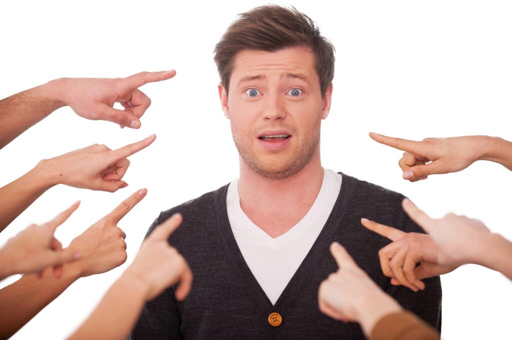 Shocked man looking at camera while many hands pointing him