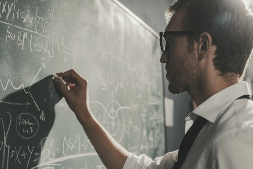 Young smart mathematician drawing math formulas on the chalkboard and thinking: he is solving problems and discovering new theories