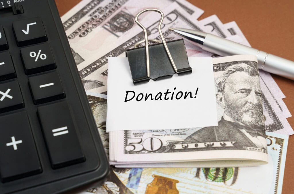 On a brown background lies a calculator and dollars on a clip with an inscription on paper - Donation