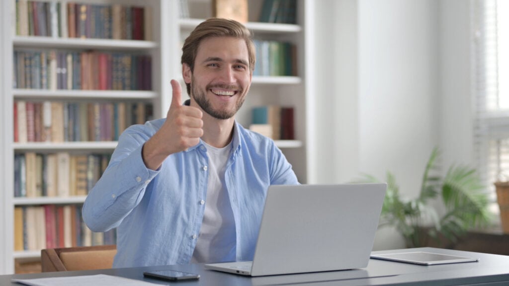 Man Showing Thumbs Up Sign While using Laptop at Work