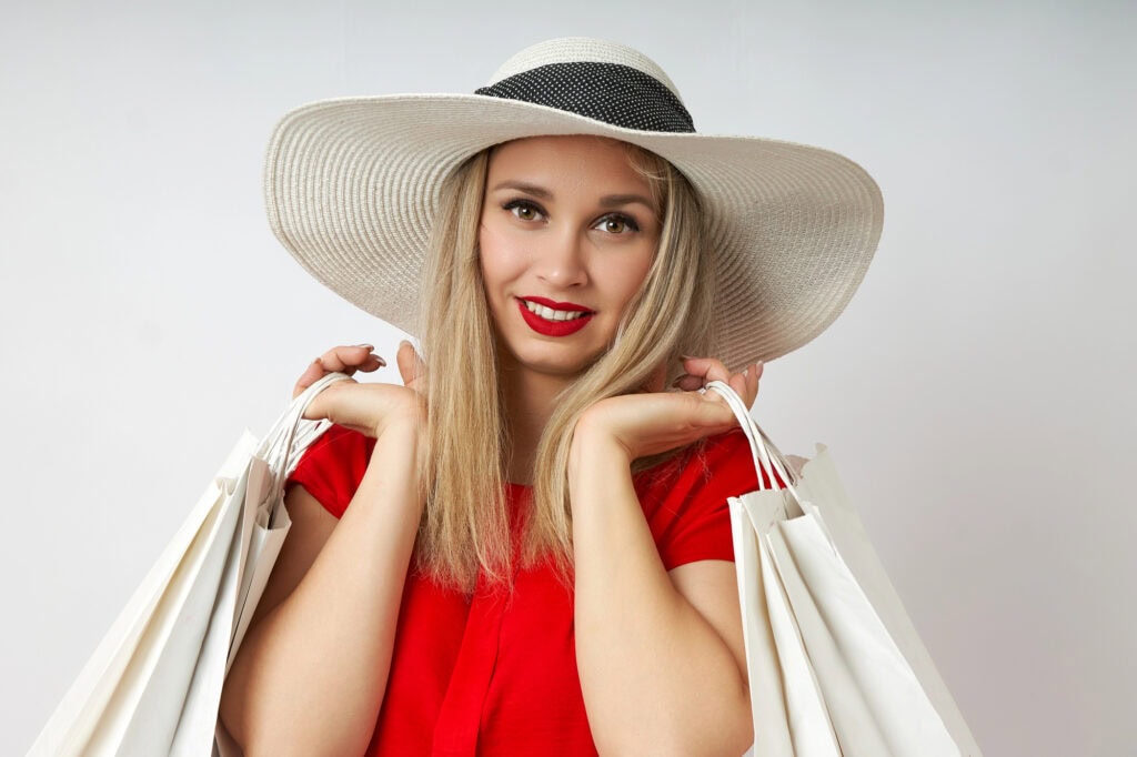 Young woman in a straw hat poses with shopping bags on a white background