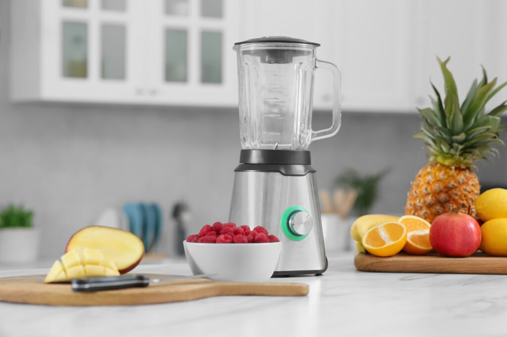 Blender and smoothie ingredients on white marble table in kitchen
