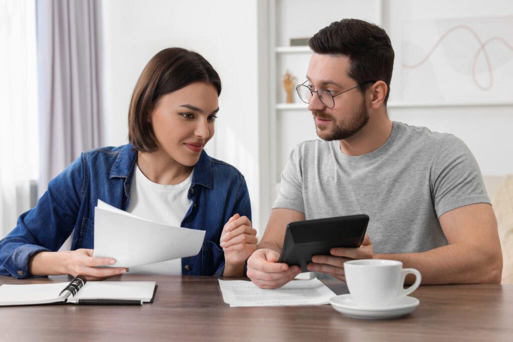 Young couple with papers discussing pension plan at wooden table indoors