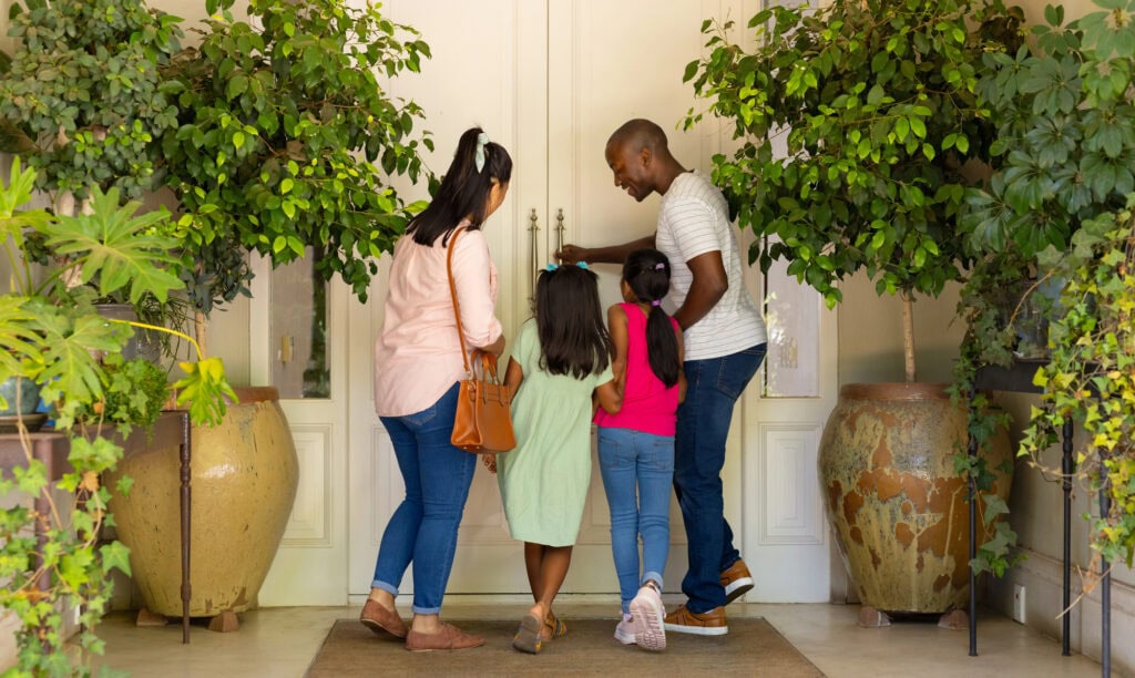 Family of four entering home, father unlocking door, children waiting eagerly.