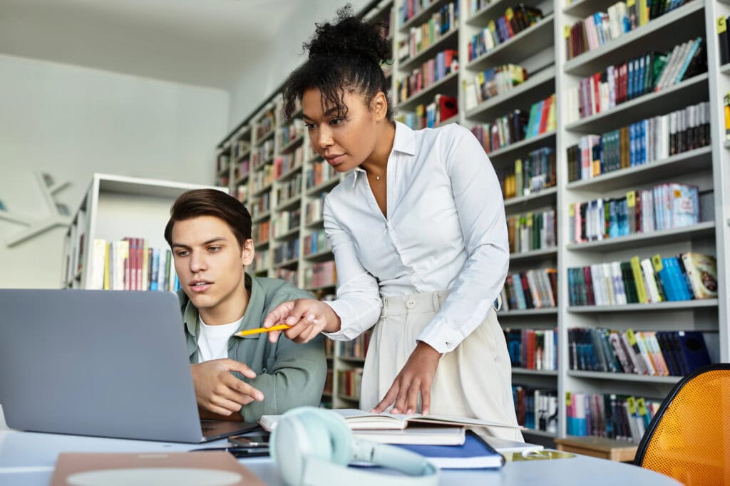 A teacher provides valuable insights while her student engages with a laptop in library