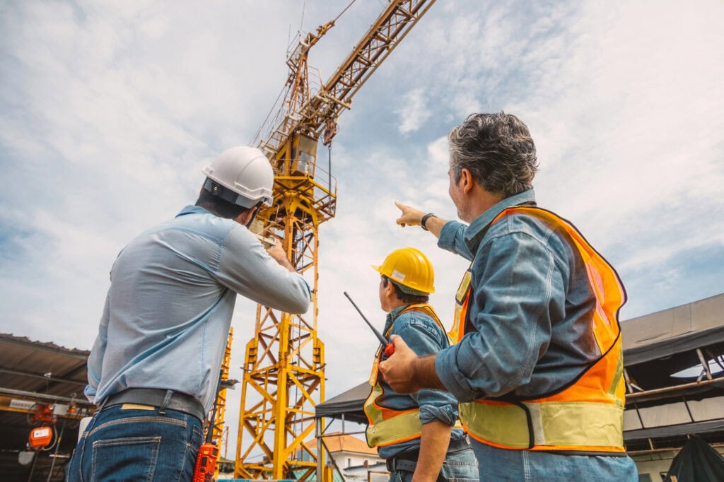 Professional construction engineer workers team working together control operating Crane tower at building project construction site.