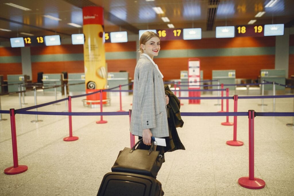 Cheerful female passenger walking with luggage to departure check in counter
