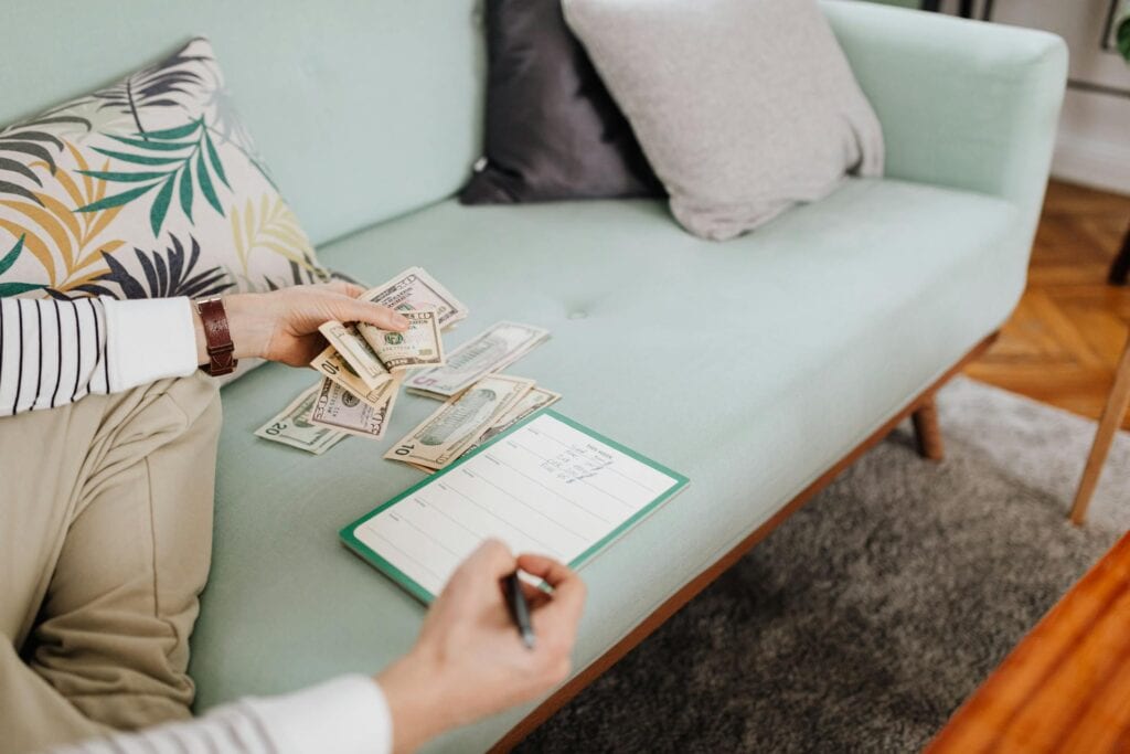 Person Writing on Paper While Counting His Money