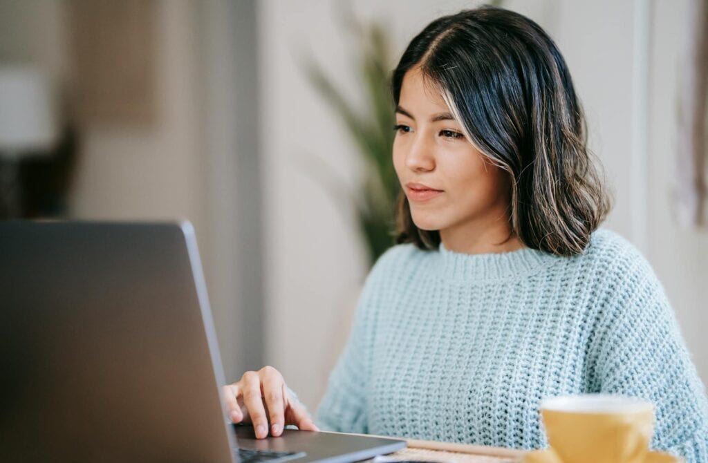 Woman using laptop near tea mug in room