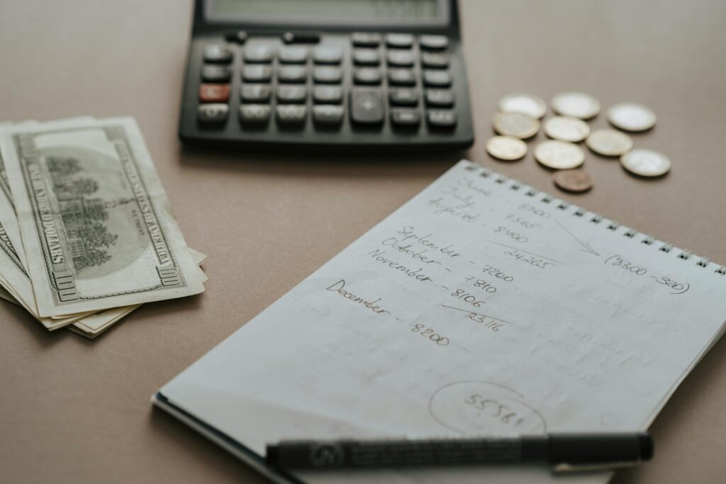 White Notebook, Calculator, dollar and coins on the Table