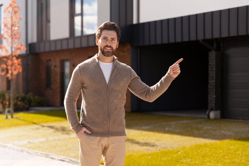 Smiling man standing outdoors pointing to a modern residential house